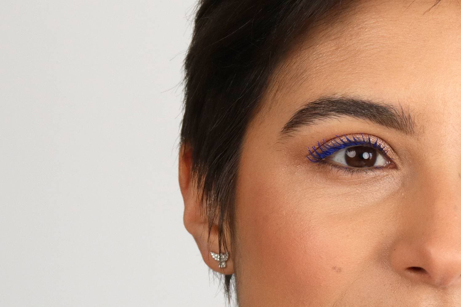 Close-up of a brown eye with electric blue mascara on the upper lashes over warm copper shimmer shadow and a groomed brow.