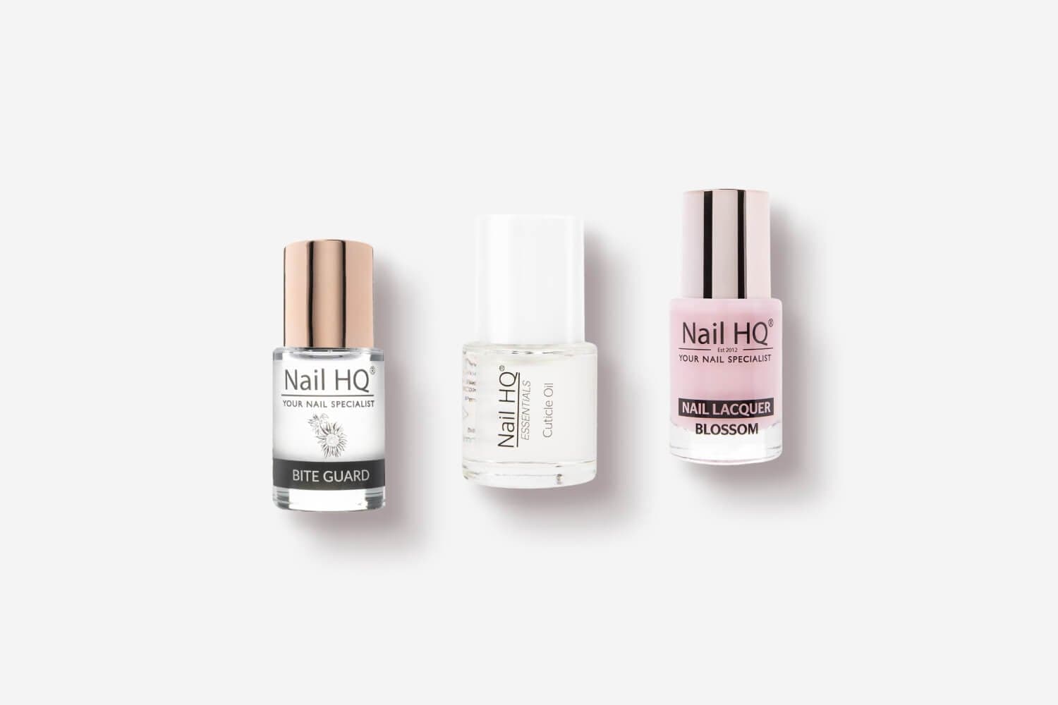 Three Nail HQ bottles on a white background: Bite Guard, Essentials Cuticle Oil and Nail Lacquer in Blossom pink.